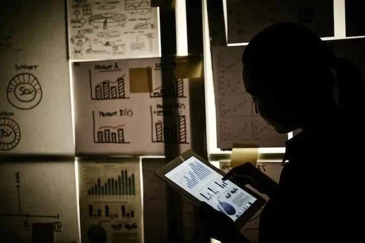 woman standing next to window covered with business charts and working on tablet